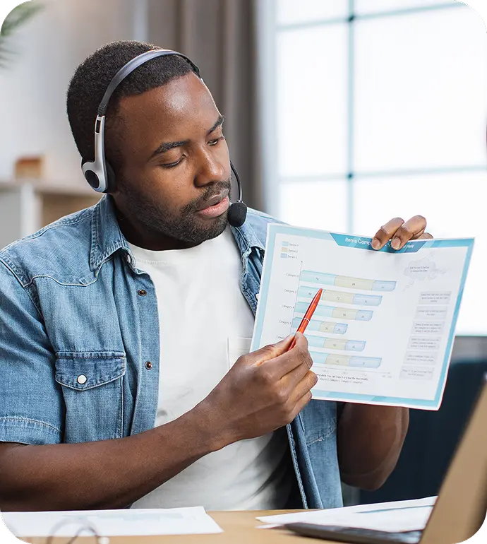 Tutor in a headset showing a chart to the camera while leading an online lesson.