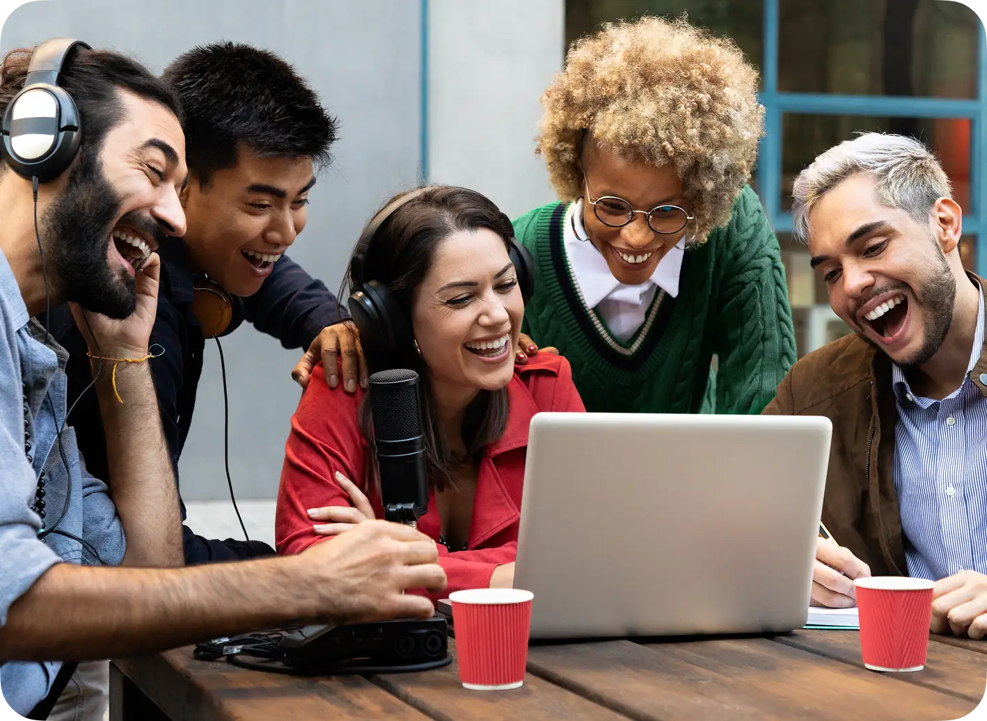Group of young adults gathered around a laptop at a shared table.