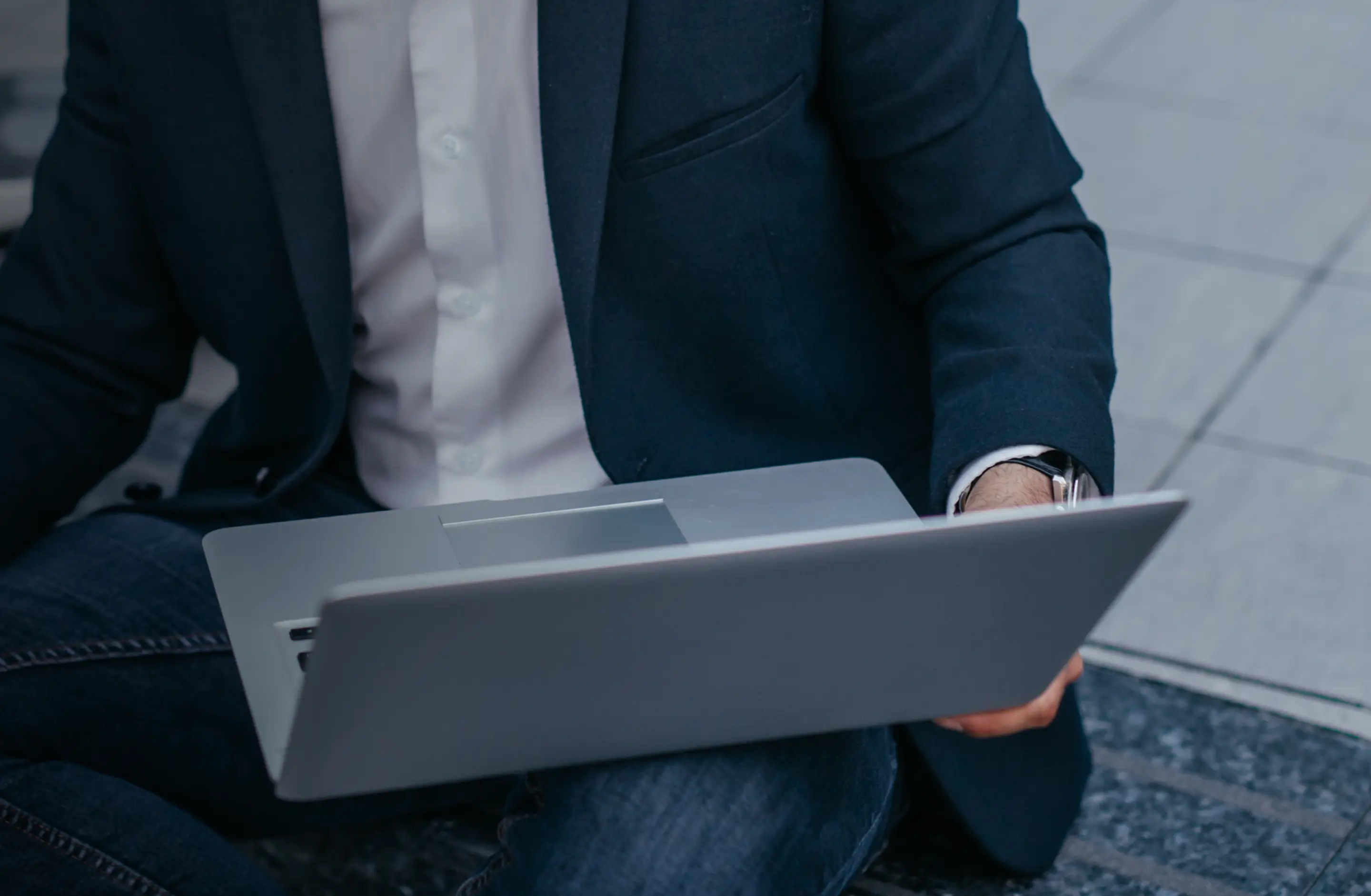 Person in a blazer sitting outdoors with an open laptop on their lap.