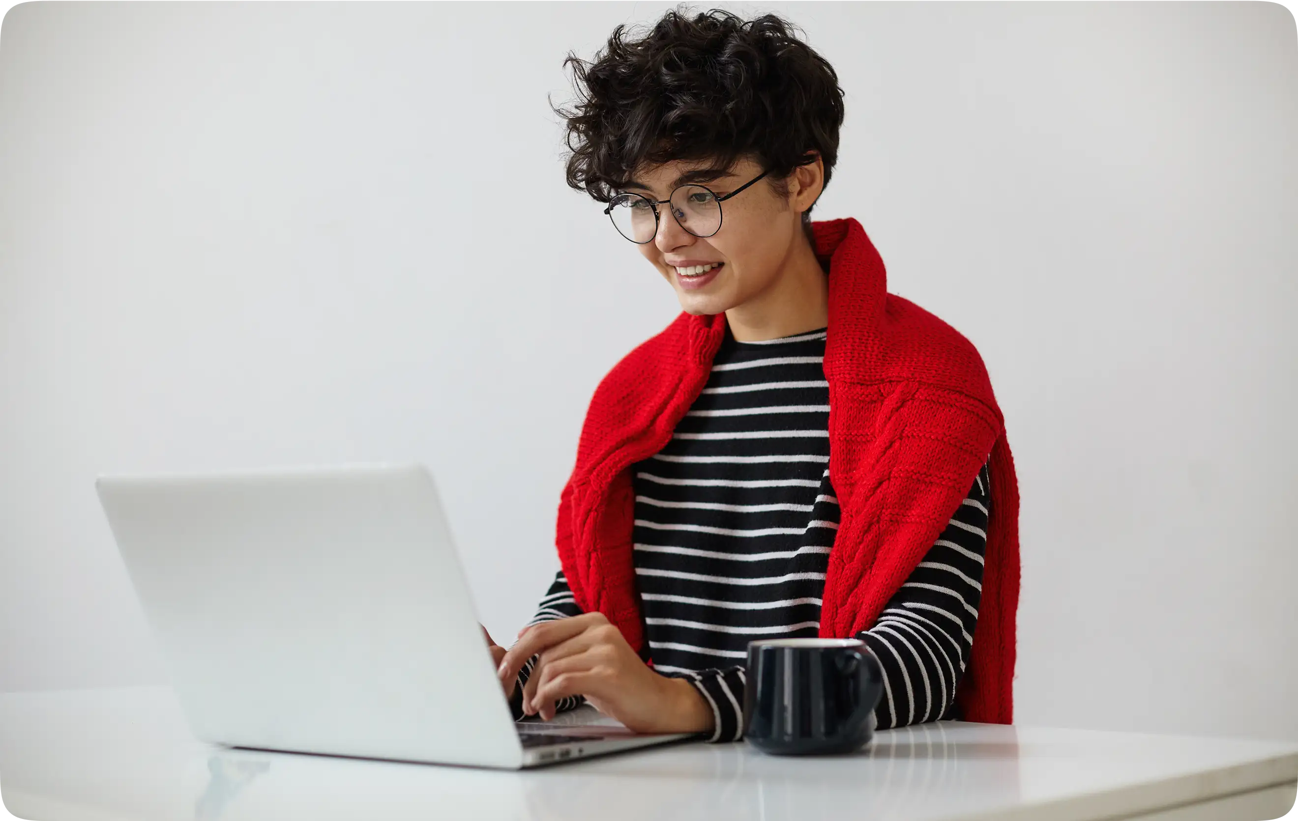 Young learner in glasses with a red sweater over the shoulders using a laptop.